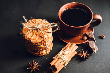 Homemade cookies, cup with hot coffee, chocolate pieces, cinnamon sticks, star anise on dark background