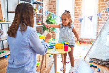 Obraz premium Caucasian girl kid playing and learning at playschool with female teacher. Mother and daughter playing cooking