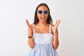 Young chinese woman wearing striped dress and sunglasses over isolated white background celebrating mad and crazy for success with arms raised and closed eyes screaming excited. Winner concept