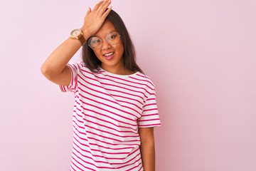Young chinese woman wearing striped t-shirt and glasses over isolated pink background surprised...