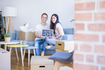 Fototapeta na wymiar Young beautiful couple sitting on the sofa holding blackboard with message at new home around cardboard boxes