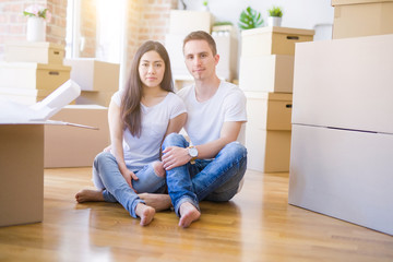Young beautiful couple sitting on the floor at new home around cardboard boxes with a confident expression on smart face thinking serious