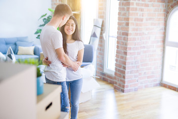 Young beautiful couple hugging at new home around cardboard boxes