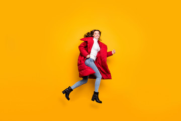 Fototapeta na wymiar Full length photo of charming lady jumping high sunny fall day rushing shopping wear jeans shoes white pullover red long winter coat isolated yellow color background