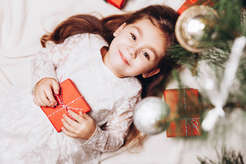 Cute happy little girl Laughing in Christmas atmosphere with gift boxes and magic lights.