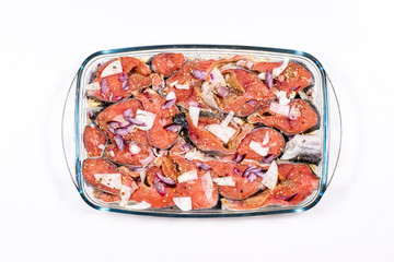 In a glass baking sheet is laid the pieces of fish underneath the potato with onions and spices, top view