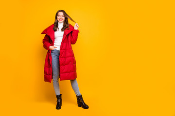 Full length photo of pretty lady traveler walking down street playing with curl wear jeans leather shoes white pullover red long winter coat isolated yellow color background - obrazy, fototapety, plakaty