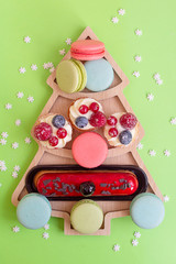 Obraz premium sweets macaroons and cakes in plate in a shape of Christmas tree, creative concept of New Year and Christmas