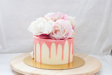 White cake with pink melted chocolate, fresh roses and peonies, macaroons and meringues. 