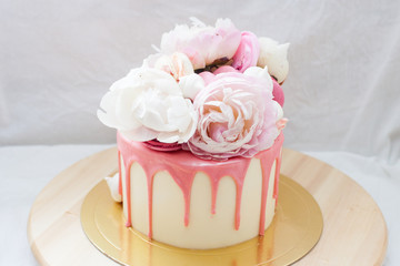 White cake with pink melted chocolate, fresh roses and peonies, macaroons and meringues. 