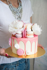 White cake with pink melted chocolate, fresh roses and peonies, macaroons and meringues. 