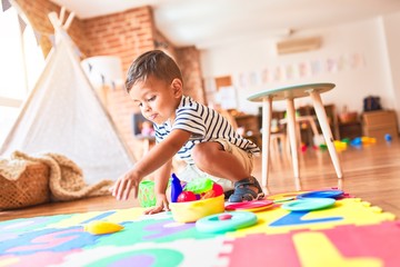 Fototapeta premium Beautiful toddler boy sitting on puzzle playing meals with plastic plates, fruits and vegetables at kindergarten