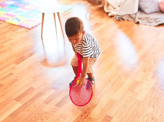 Beautiful toddler boy playing tennis with red racket and ball at kindergarten