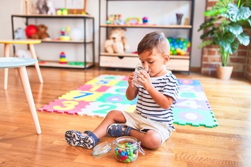 Beautiful toddler boy drinking glass of water at kindergarten