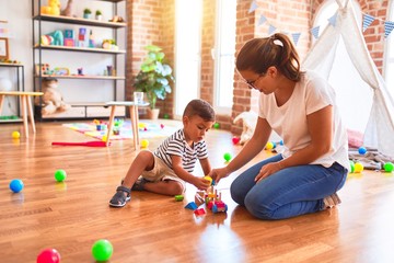 Fototapeta premium Beautiful teacher and toddler boy playing with train at kindergarten