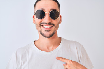 Young handsome man wearing sunglasses and casual t-shirt over isolated background with surprise...