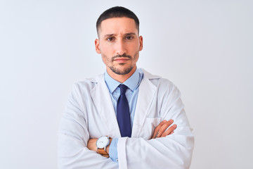 Young doctor man wearing white coat over isolated background skeptic and nervous, disapproving expression on face with crossed arms. Negative person.