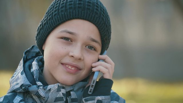 Happy kid in a knitted hat chatting with his father on a phone outdoors in autumn