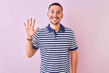 Fototapeta premium Young handsome man wearing nautical striped t-shirt over pink isolated background showing and pointing up with fingers number five while smiling confident and happy.