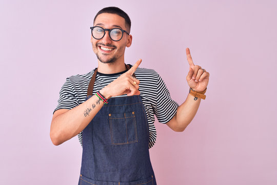 Young handsome man wearing employee apron over isolated background smiling and looking at the camera pointing with two hands and fingers to the side.
