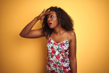 African american woman wearing floral summer t-shirt over isolated yellow background very happy and smiling looking far away with hand over head. Searching concept.