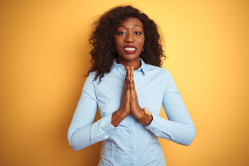 African american businesswoman wearing elegant shirt over isolated yellow background praying with hands together asking for forgiveness smiling confident.
