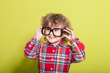 Portrait of a little curly boy in glasses on a bright green background. Little scientist, inventor, researcher, physicist, mathematician.