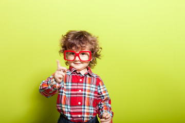 Portrait of a little curly boy in glasses on a bright green background. Little scientist, inventor,...