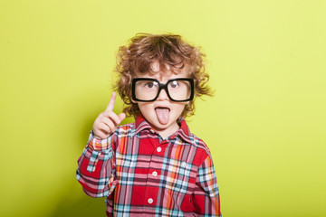 Portrait of a little curly boy in glasses on a bright green background. Little scientist, inventor,...