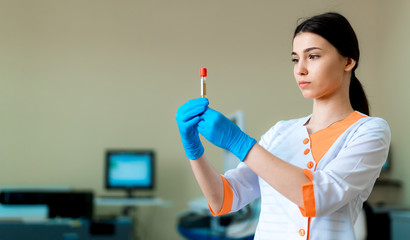 Brunette female doctor is holding red blood in test tube on clinic blurred background. health...