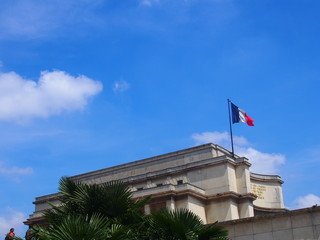 Fototapeta na wymiar The French flag fluttering in the wind next to the building under blue skies, Paris, France