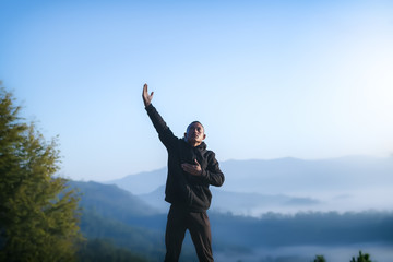 A man lift hand and praying to God at morning on mountains with nature landscape. Christian concept.