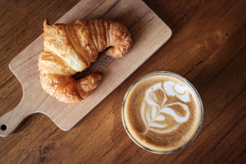 A cup of coffee with latte art on top and butter  croissant