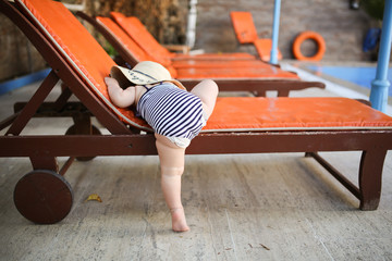 baby in swimsuit and diaper climbs on deck chair