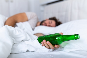 Unconscious drunk man with bottle of alcohol in hands sleeping in bed . Alcoholism problem and...