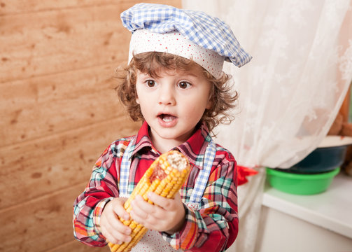 Portrait of a crispy boy in chef clothes in the kitchen interior. Child culinary busy preparing food.
