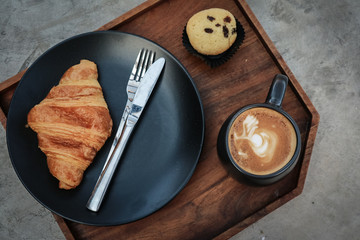 A cup of coffee with latte art on top and butter  croissant