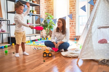 Beautiful teacher and toddler playing around lots of toys at kindergarten