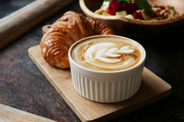 A cup of coffee with latte art on top, butter  croissant and granola with fresh tropical fruits and...