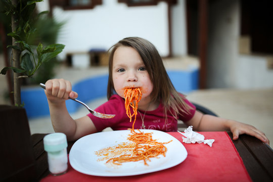dirty girl child eating pasta with tomato sauce