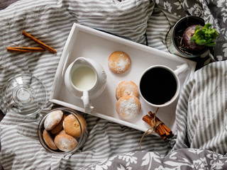 A beautiful white wooden tray with coffee, cookies and cream in a jug, on a gray background. breakfast concept in bed.