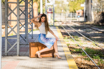 Chica morena posando con maleta en arcén de estación de tren