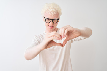 Plakat Young albino blond man wearing t-shirt and glasses standing over isolated white background smiling in love showing heart symbol and shape with hands. Romantic concept.