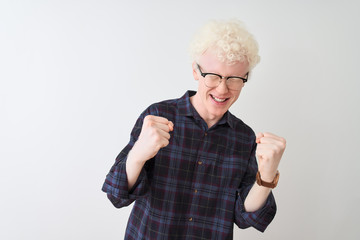 Young albino blond man wearing casual shirt and glasses over isolated white background very happy and excited doing winner gesture with arms raised, smiling and screaming for success. Celebration 