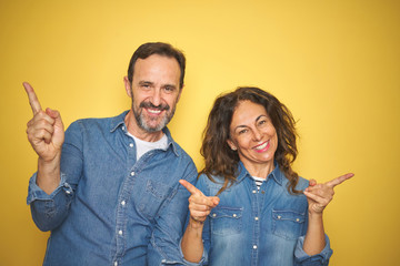 Beautiful middle age couple together standing over isolated yellow background smiling confident pointing with fingers to different directions. Copy space for advertisement