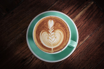 A cup of coffee with latte art on top on dark wooden background, top view