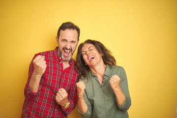 Beautiful middle age couple over isolated yellow background very happy and excited doing winner gesture with arms raised, smiling and screaming for success. Celebration concept.