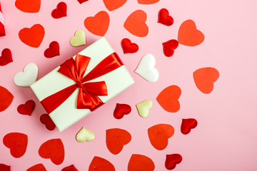 Valentines day flat lay copy space. On a pink background, a gift box and a red bow, red paper hearts, hearts made of white fabric and red satin will create a frame for text. Copy space.