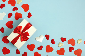 Valentine's Day background flat lay copy space. On a blue background, a frame for text from red and white hearts, a box with a gift with a red ribbon.