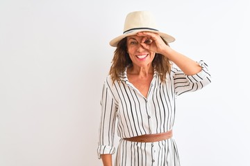 Obraz na płótnie Canvas Middle age businesswoman wearing striped dress and hat over isolated white background doing ok gesture with hand smiling, eye looking through fingers with happy face.